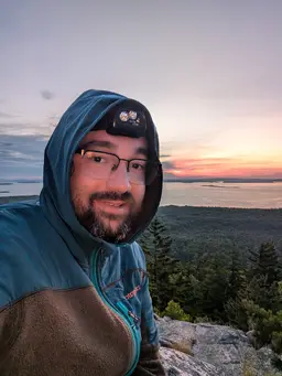 Closeup image of Tyler's face, on top of a coastal mountain overlooking a harbor at sunset. He's very handsome
